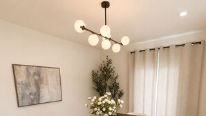 A dining room with a long wooden table, white chairs, a vase with flowers, a painting on the wall, and a ceiling light fixture. - •4BR·3BA Miami Oasis, Big Yard, Pool & Jacuzzi, Perfect for Vacations & Events• (Miami)