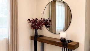 A modern interior with a wooden console table, a mirror, and a vase with red leaves. - •4BR·3BA Miami Oasis, Big Yard, Pool & Jacuzzi, Perfect for Vacations & Events• (Miami)