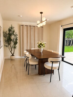 Uma sala de jantar moderna com mesa de madeira, seis cadeiras, um vaso de plantas e um arranjo de flores.