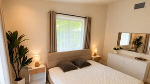 Een moderne slaapkamer met een groot bed, bedlampen, een nachtkastje, een kamerplant en een raam met gordijnen.