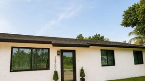 Een modern huis met een verharde oprit, een groot raam en een deur met een nummer op de gevel.