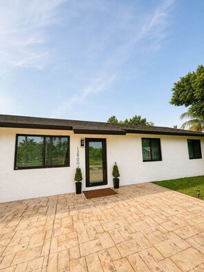 Uma casa moderna com calçada pavimentada, uma janela grande e uma porta com um número na parede.