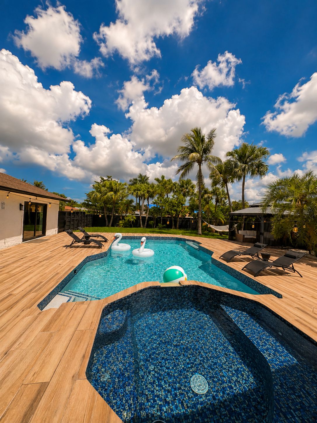 Une piscine avec des bouées en forme de cygne et un décor tropical agrémenté de palmiers.