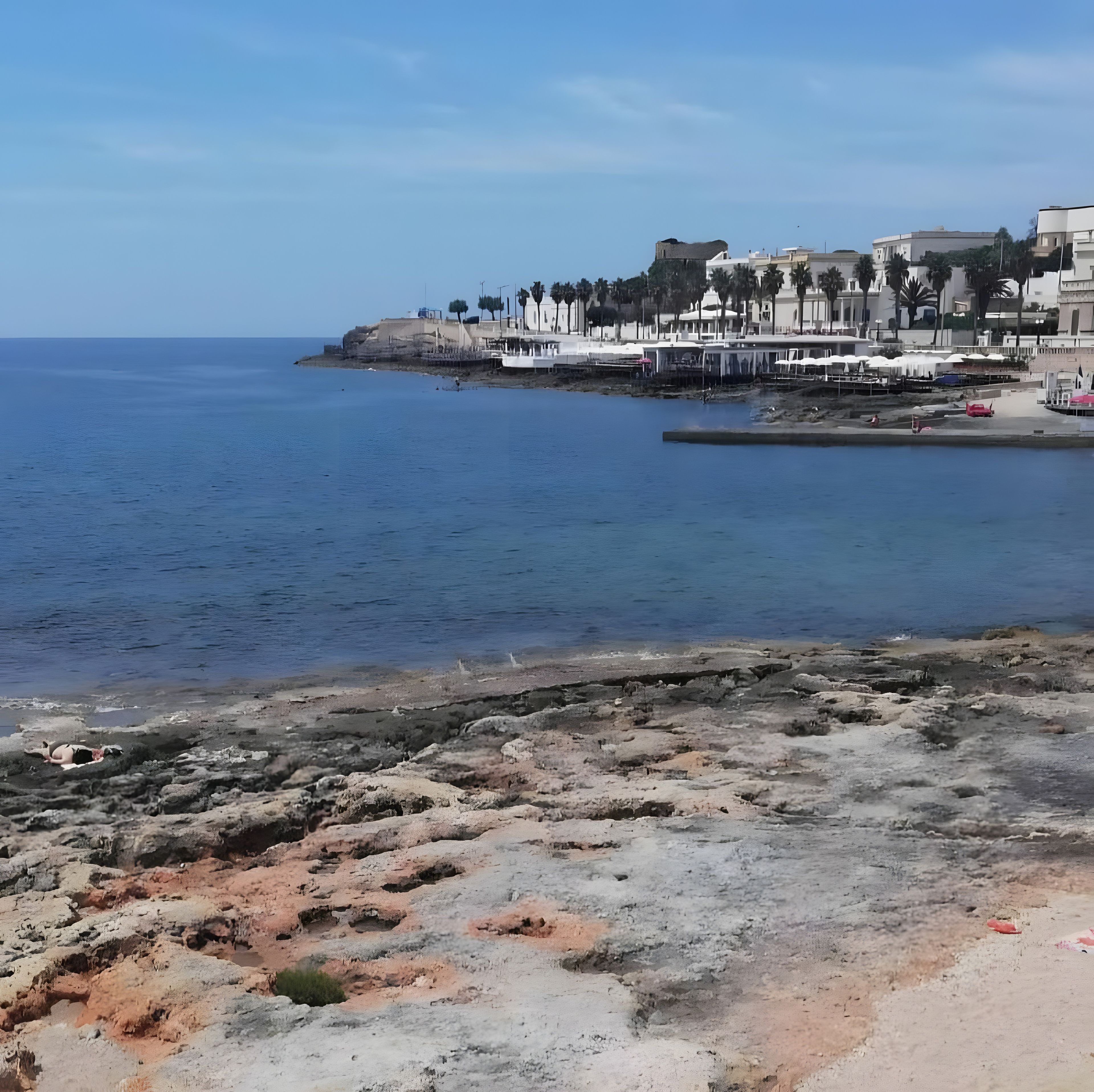 Una zona costera con un litoral rocoso, un paseo marítimo con edificios y un cielo despejado.