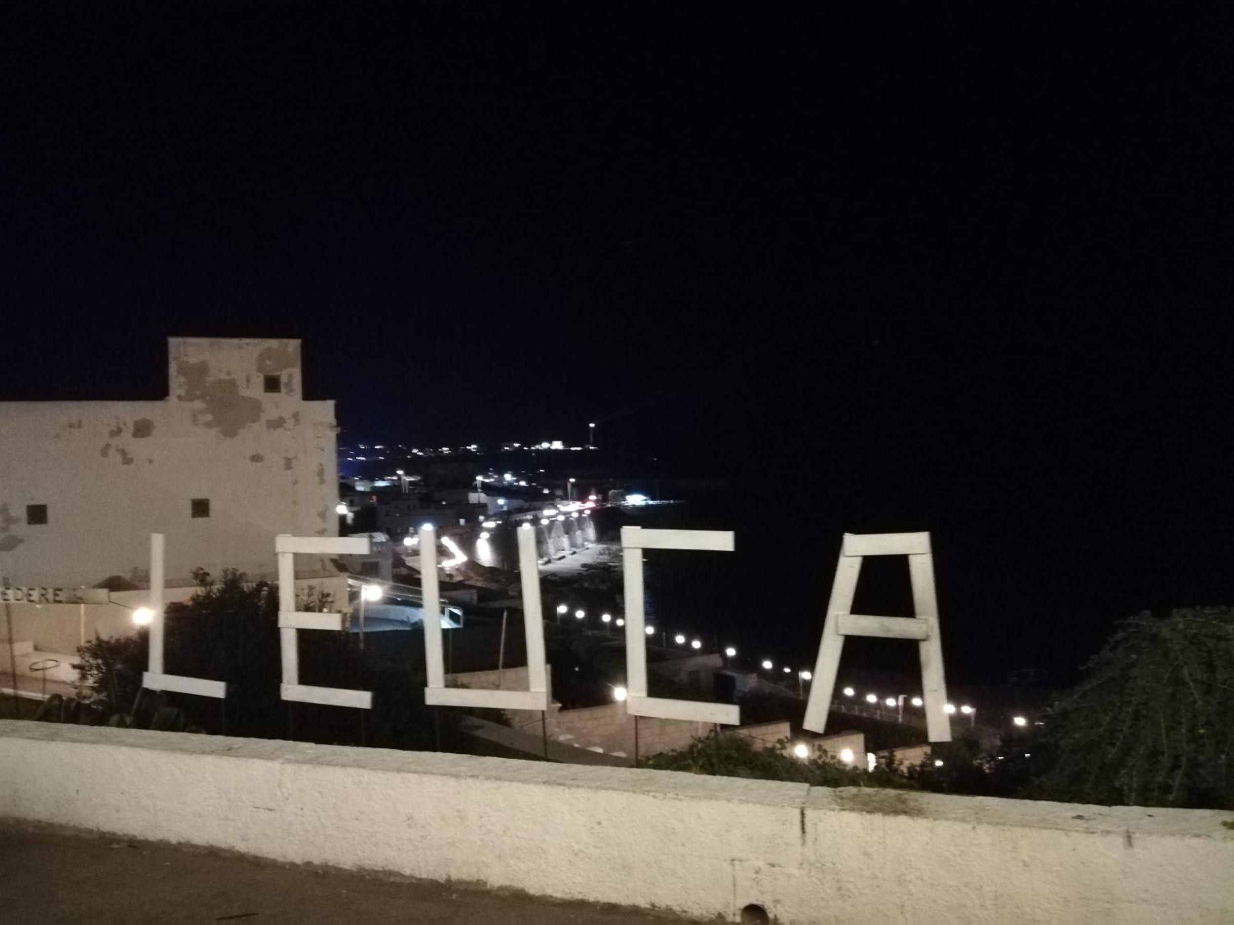 Una vista notturna di un paesaggio urbano illuminato da lampioni e con un edificio dove si legge chiaramente 'LEUCA'.