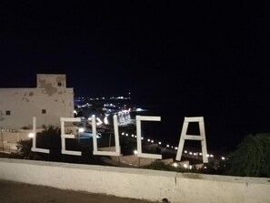 A nighttime view of a cityscape with illuminated street lights and a building with the word 'LEUCA' displayed prominently. - Apartment 'Amata Villa Vacanza' with Private Garden, Wi-Fi and Air Conditioning (Santa Maria di Leuca)