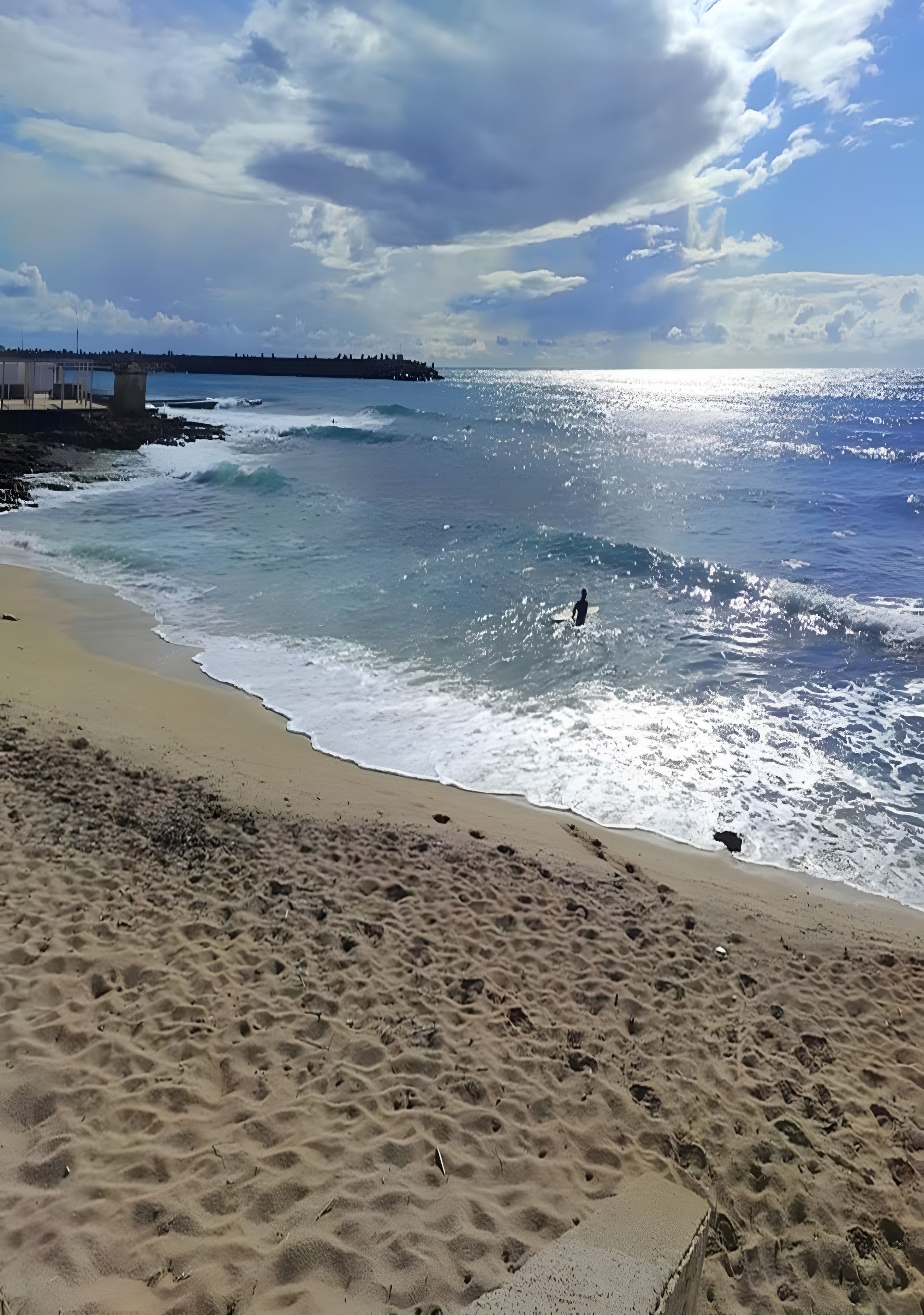 Une plage avec des vagues, un ciel dégagé et une côte lointaine.