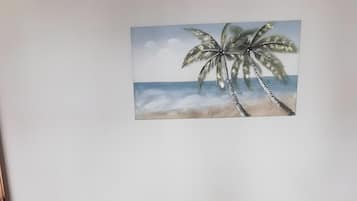 Un lit avec un matelas et une tête de lit, un mur orné d’un tableau et un sol carrelé.