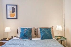 Une chambre d’hôtel avec un lit, deux lampes de chevet, une œuvre d’art encadrée au mur et une fenêtre.
