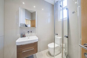 A modern bathroom with a glass shower enclosure, a white sink with a wooden vanity, and a toilet. - Fitzrovia 1BR Retreat | Near Soho & Tube-7 (Greater London)