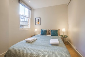 A hotel room with a large bed, two bedside tables, a window with a view, and a framed picture on the wall. - Fitzrovia 1BR Retreat | Near Soho & Tube-7 (Greater London)