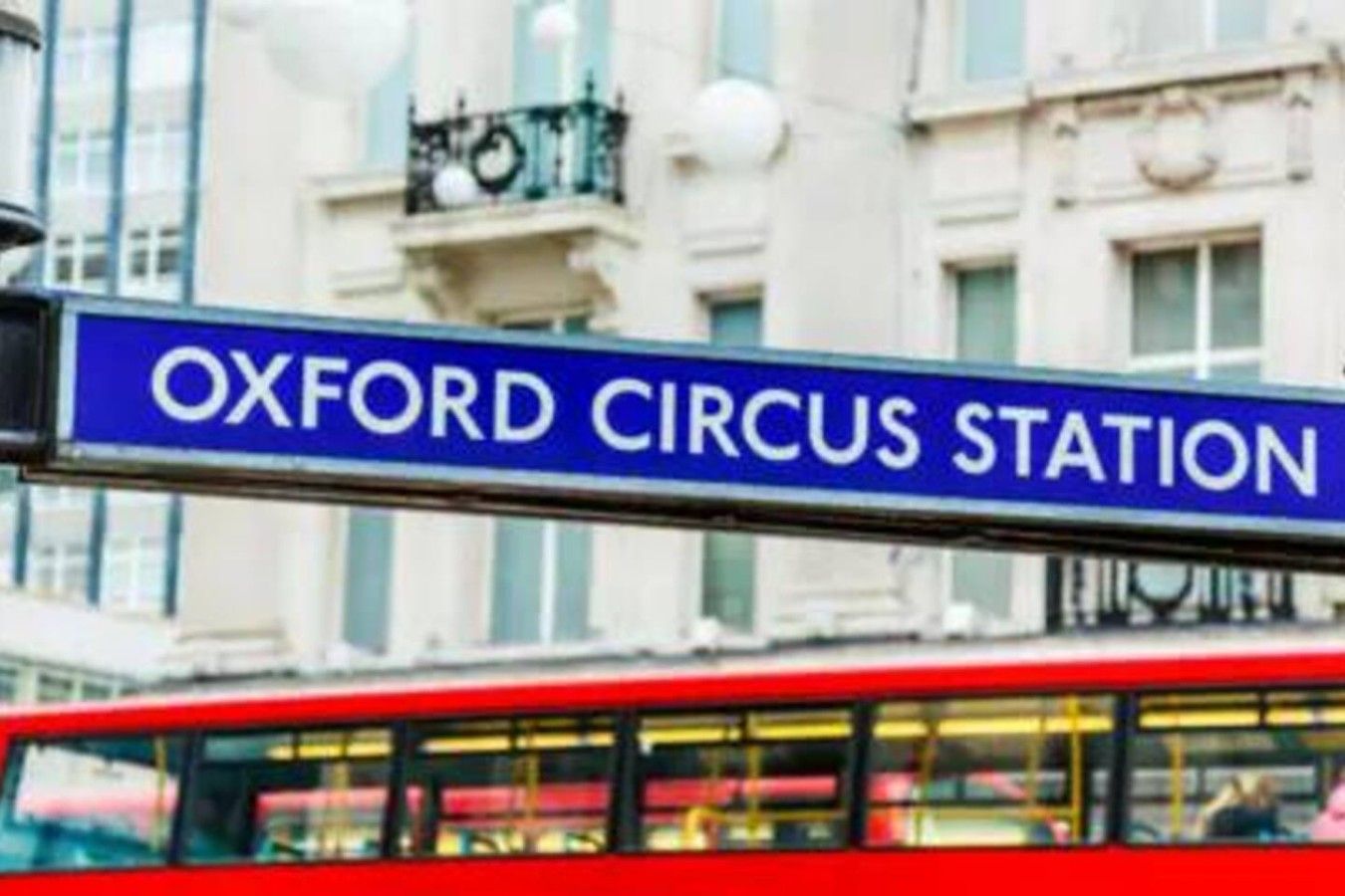 Et skilt der angiver 'Oxford Circus Station', med en rød, tosset bus i baggrunden.