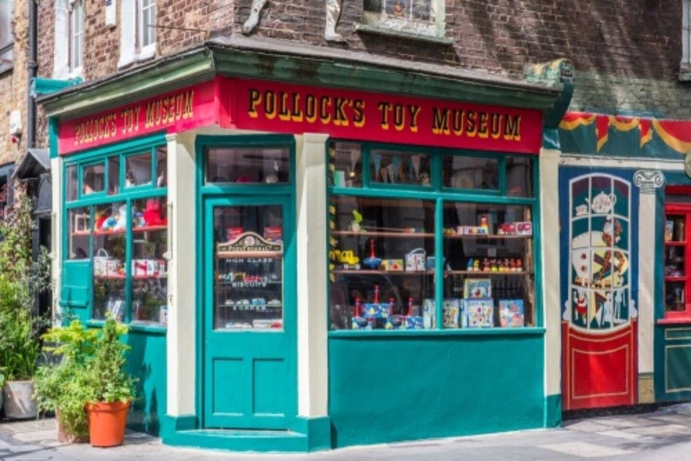 Un museo de juguetes con un letrero rojo, fachada color verde azulado y escaparates de vidrio.
