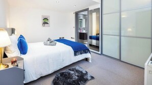 Una habitación de hotel moderna con una cama, una mesita de noche, una lámpara, una pequeña mesa con una vela y una alfombra.