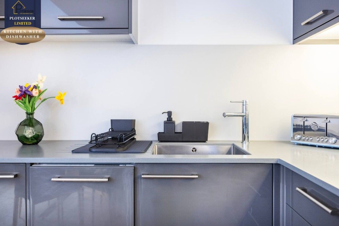 A modern kitchen with a built-in dishwasher, a stainless steel sink, and a toaster.