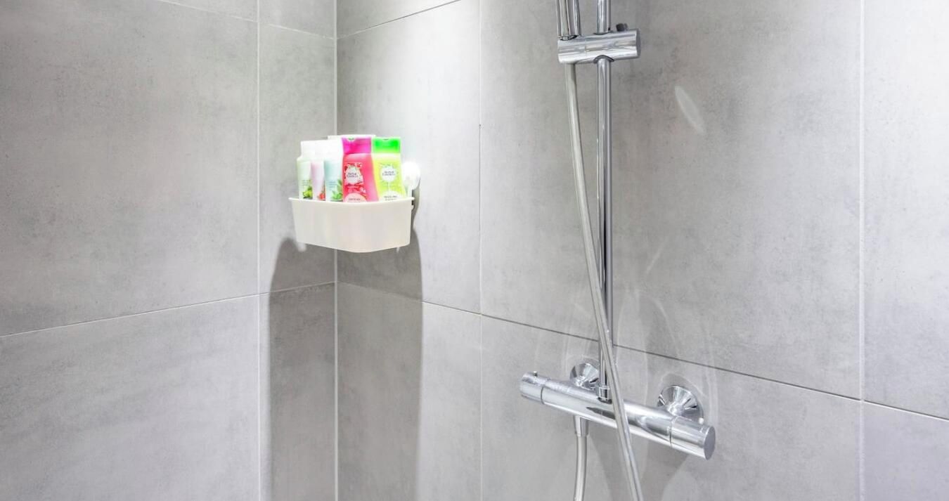 A shower area with a chrome showerhead and a wall-mounted soap dispenser.