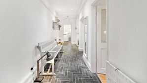 A narrow hallway with a herringbone floor pattern, white walls, and a bench with a lamp. - Victorian 3BR | 1-Min Tube | Work Ready (Greater London)