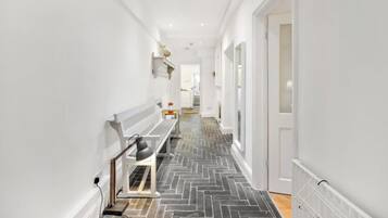 A narrow hallway with a herringbone floor pattern, white walls, and a bench with a lamp.