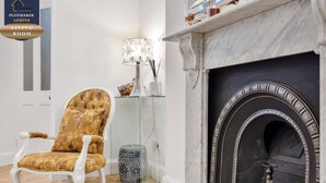 A living room with a fireplace, a tufted armchair, and a modern lamp. - Victorian 3BR | 1-Min Tube | Work Ready (Greater London)