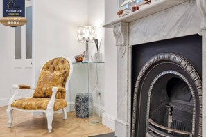A living room with a fireplace, a tufted armchair, and a modern lamp. - Victorian 3BR | 1-Min Tube | Work Ready (Greater London)