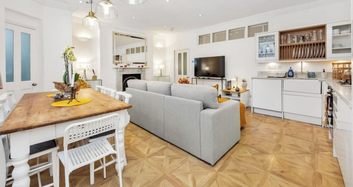 A modern living room with a grey sofa, a wooden dining table, and a TV.