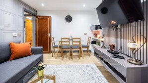 Een moderne woonkamer met een bank, een eettafel, stoelen, een flatscreen televisie en een decoratieve lamp.