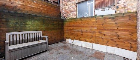 Une cour avec un banc, un mur en briques et une fenêtre.