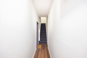 Ein schmaler Flur mit Holzboden führt zu einer Treppe mit dunklen Stufen.