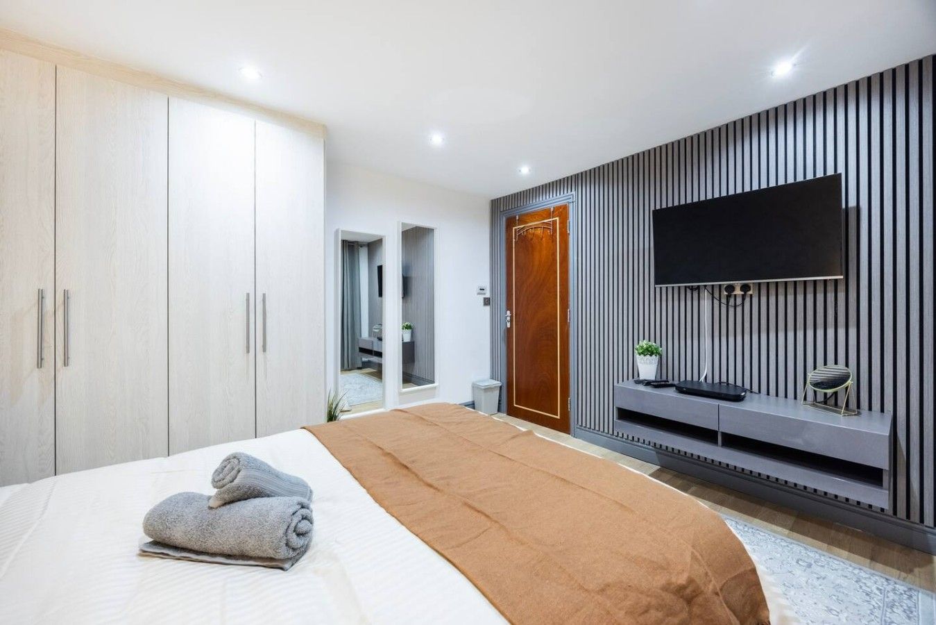Un dormitorio moderno con una cama grande, un televisor montado en la pared y un armario.