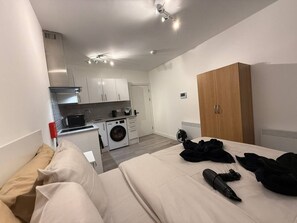 A compact hotel room with a kitchenette, a washing machine, and a bed with a blanket and a remote control. - Cosy Room | Easy Access to Central London (Greater London)