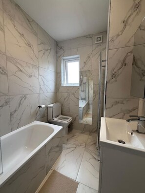 Ein Badezimmer mit Badewanne, Toilette und Duschbereich, mit Marmorwänden und Fliesenboden.