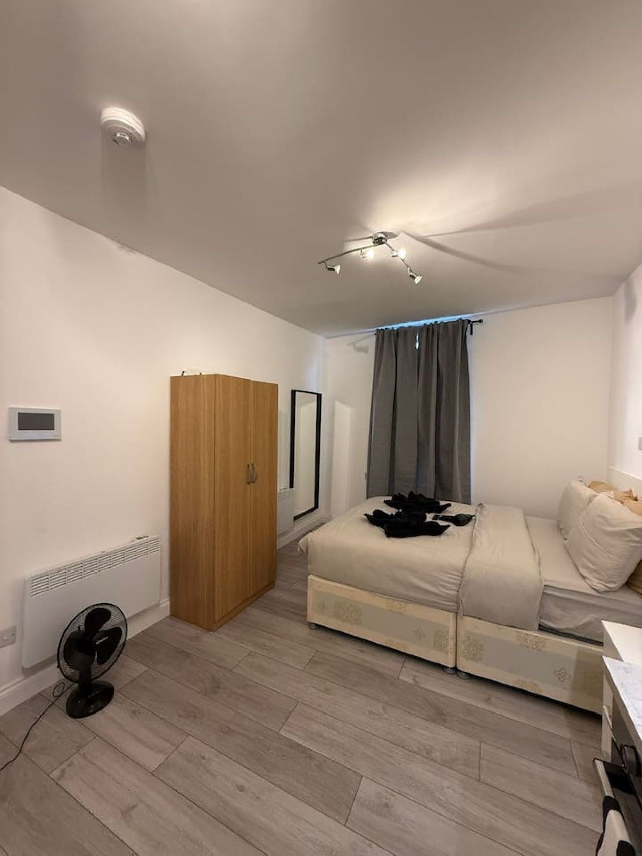 A bedroom with a bed, a wardrobe, a ceiling fan, and a window with curtains.