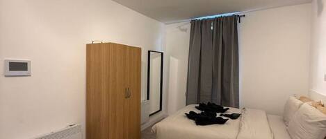A bedroom with a bed, a wardrobe, a ceiling fan, and a window with curtains.