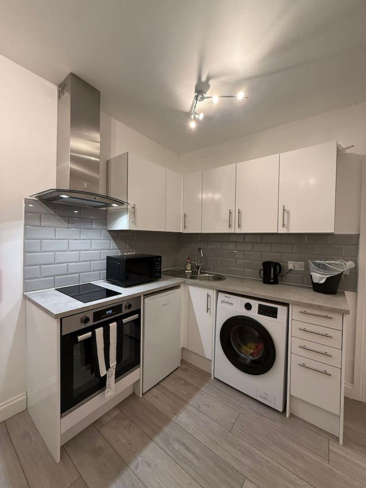 Une cuisine compacte avec des meubles blancs, un four à micro-ondes, un four traditionnel, un lave-linge et un évier.