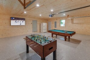 Une pièce équipée d’un baby-foot, d’une table de billard et d’un écran de projection diffusant un événement sportif.
