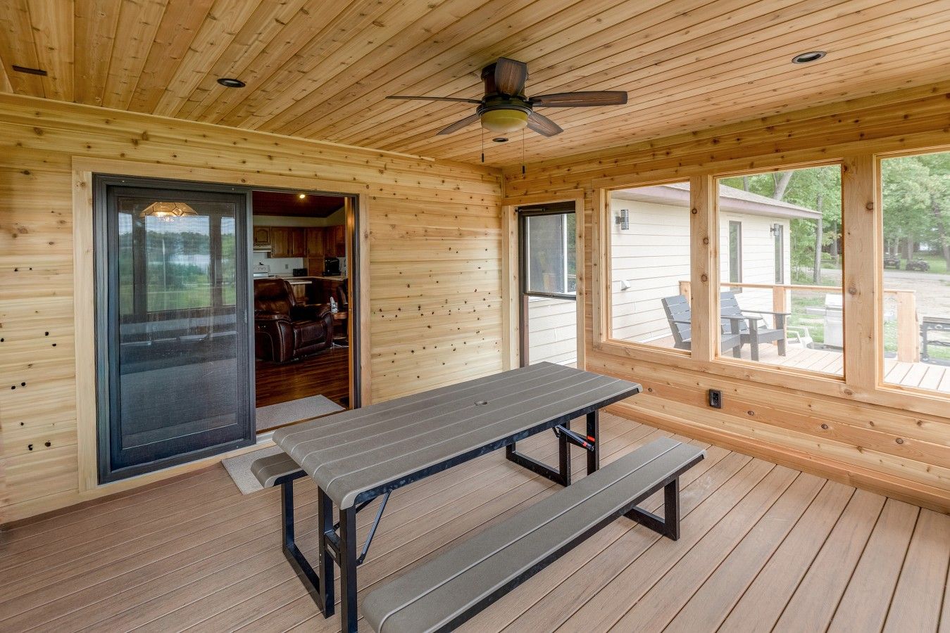 A wooden interior with a table and benches, large windows, and a ceiling fan.