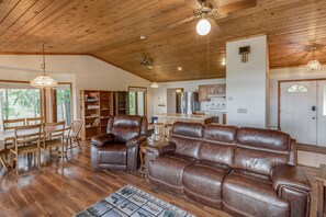 A spacious living room with a leather sofa, wooden dining table, and chairs.