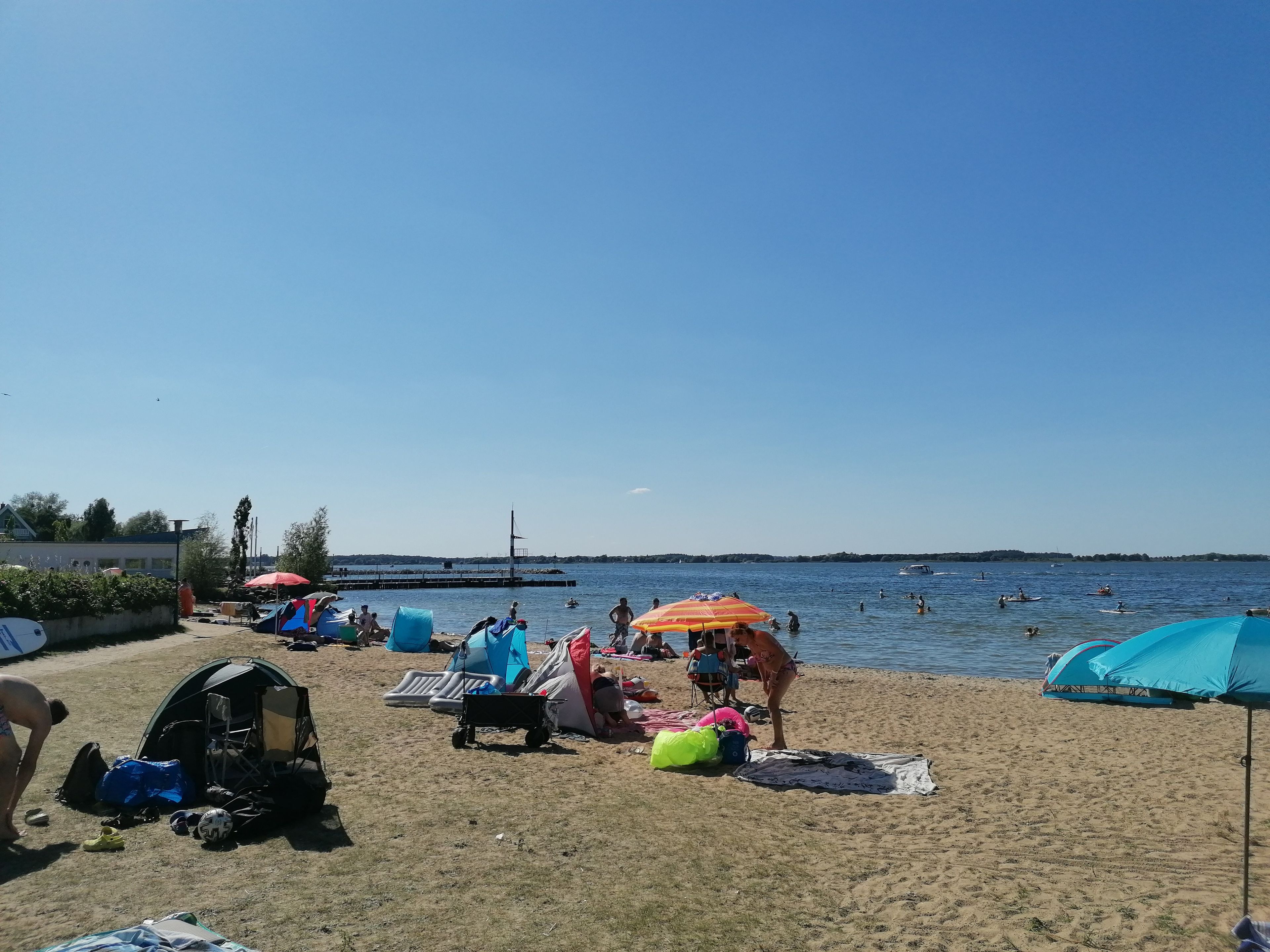Une plage avec des tentes, des parasols et des personnes pratiquant des activités nautiques.