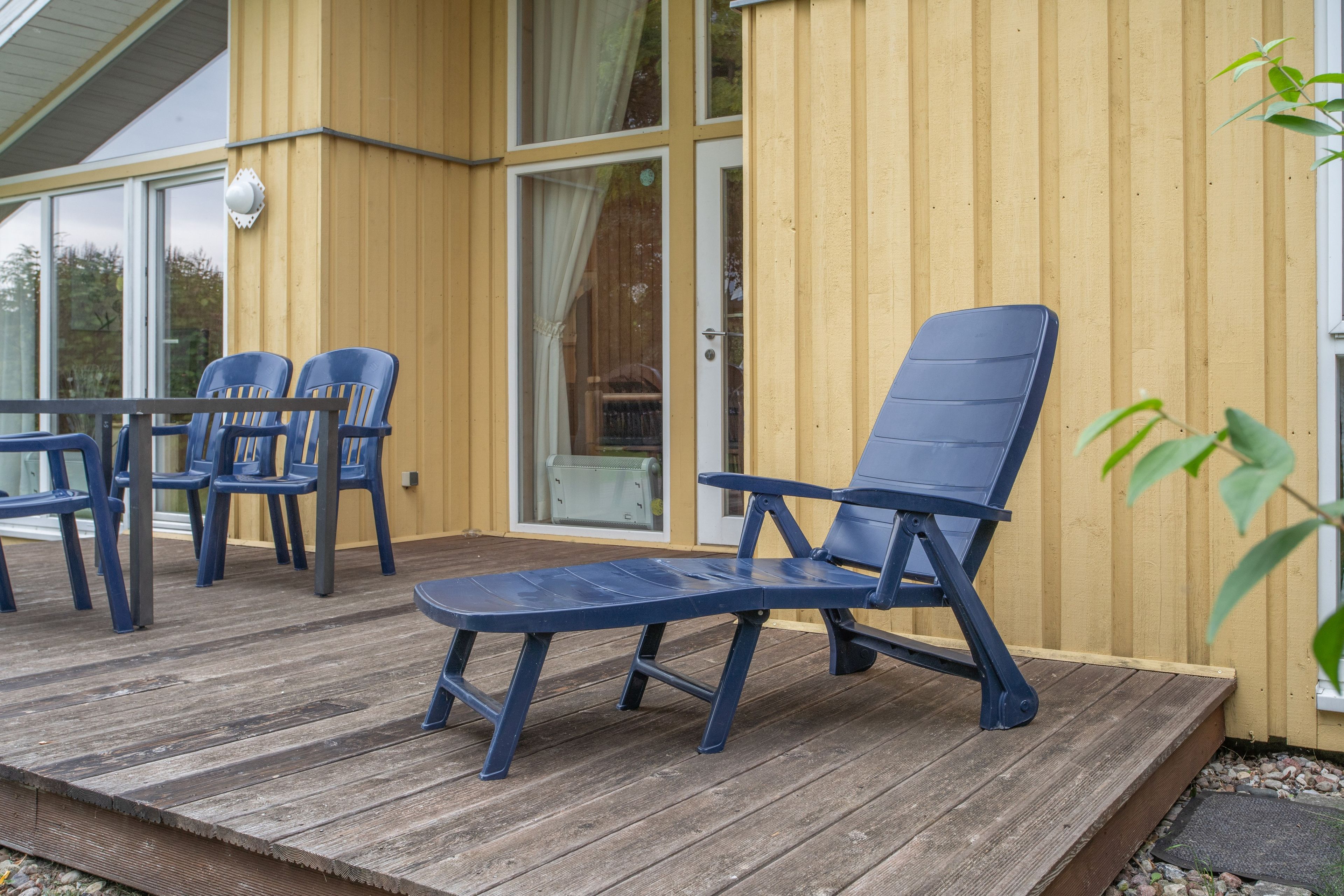 Eine Terrasse mit blauen Stühlen und einem Tisch, Holzboden und eine gelbe Gebäudefassade.