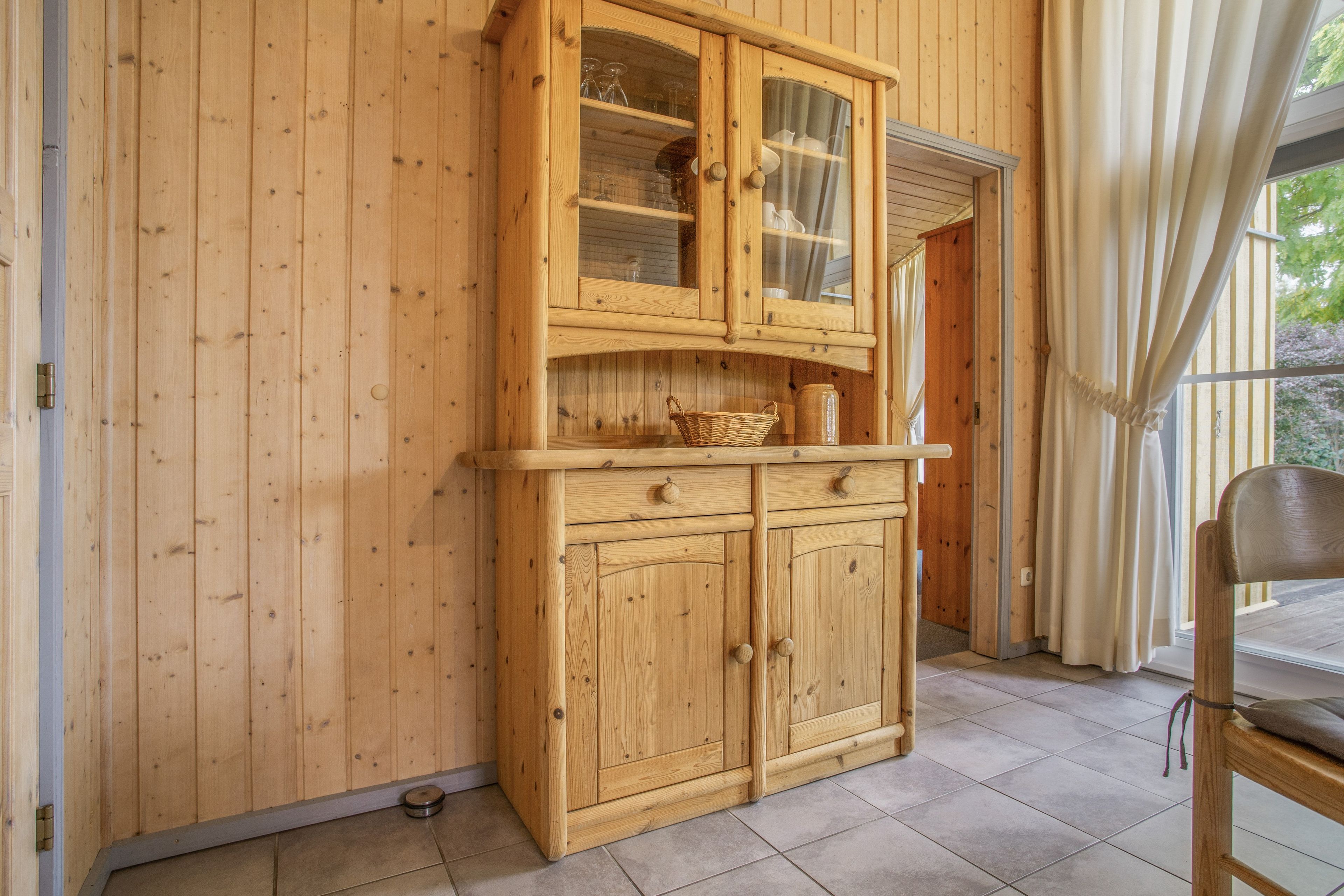 Un meuble en bois avec des portes en verre, un panier en osier et un petit pot sur le comptoir.