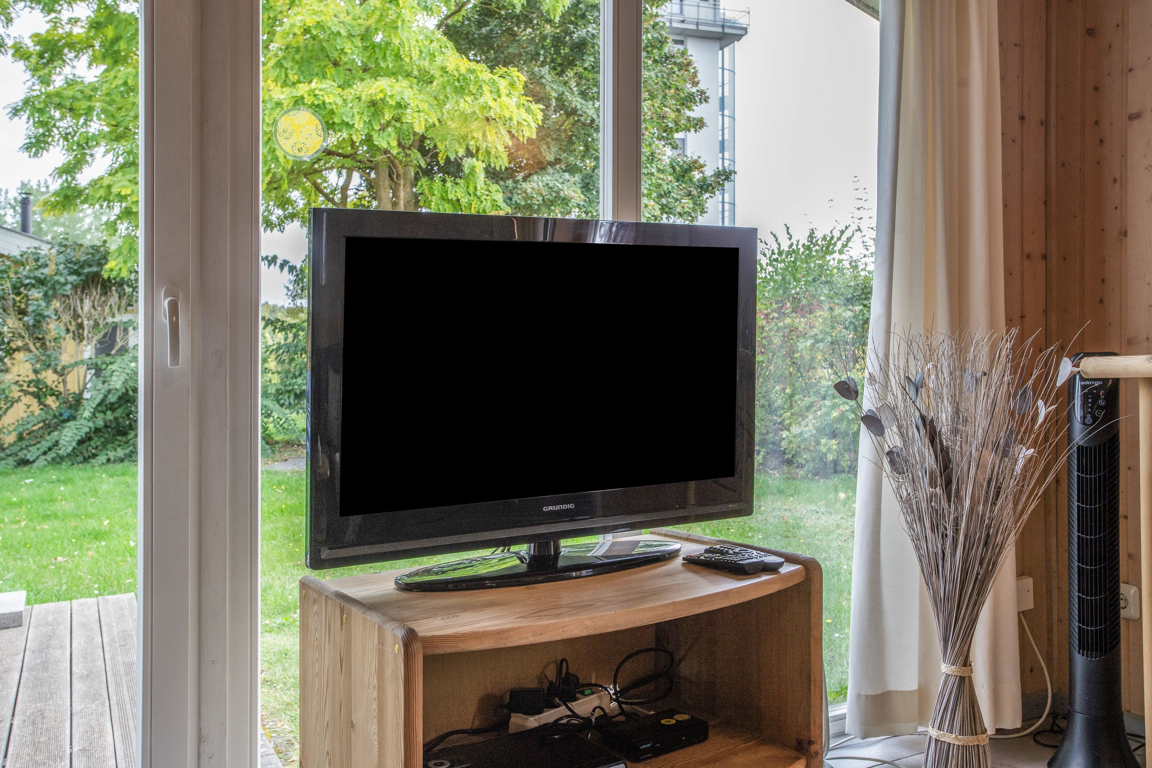 Un televisor sobre un atril de madera en una habitación con vistas a un jardín.