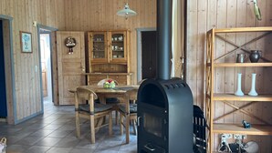 En inredning med träpanel, ett bord i mitten, stolar, en öppen spis och en hylla med dekorativa föremål.