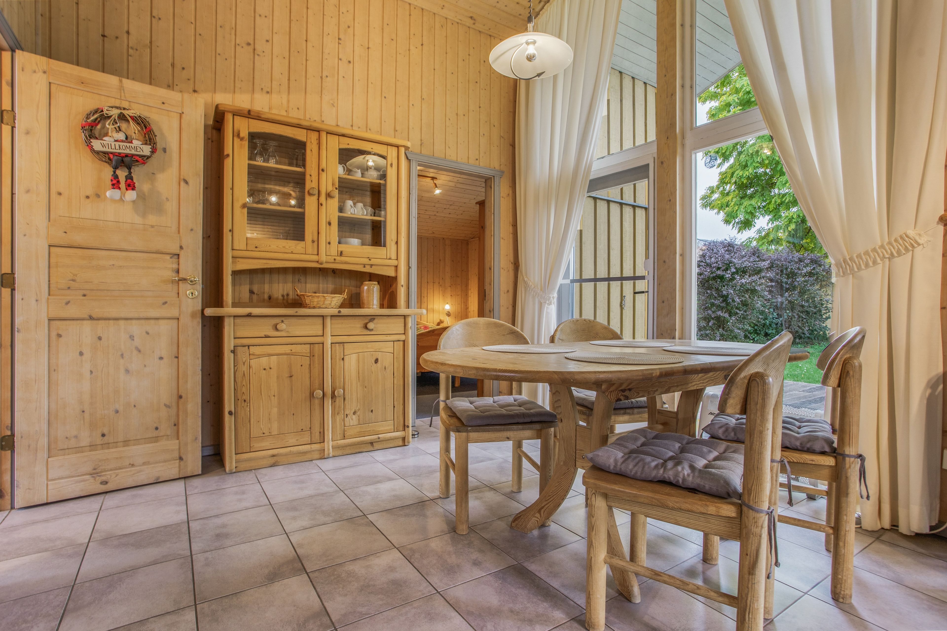 Un intérieur en bois comprenant une table à manger et des chaises, un meuble avec des portes en verre et une fenêtre avec des rideaux.