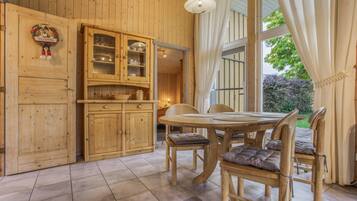 Un interior de madera con una mesa de comedor y sillas, un armario con puertas de cristal, y una ventana con cortinas.