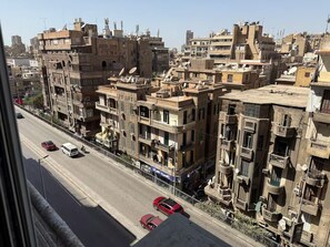 Una calle urbana densamente poblada con edificios de varios pisos, algunos con balcones, y algunos automóviles en la vía.