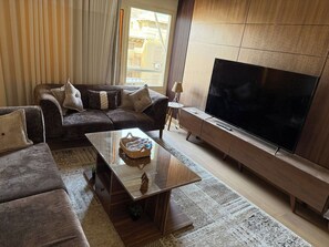 Ein Wohnzimmer mit einer Couch, einem Couchtisch, einem Fernseher und einem großen Fenster mit Jalousien.