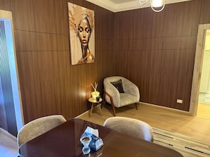 Ein Essbereich mit einer holzverkleideten Wand, einem Gemälde, einem kleinen Tisch mit Kerze und einem Stuhl.