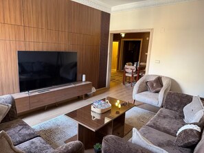 A modern living room with a large flat-screen TV, a wooden entertainment unit, and a seating area with two sofas and a coffee table. - 2BR Apartment in downtown Zamalek (Cairo Governorate)