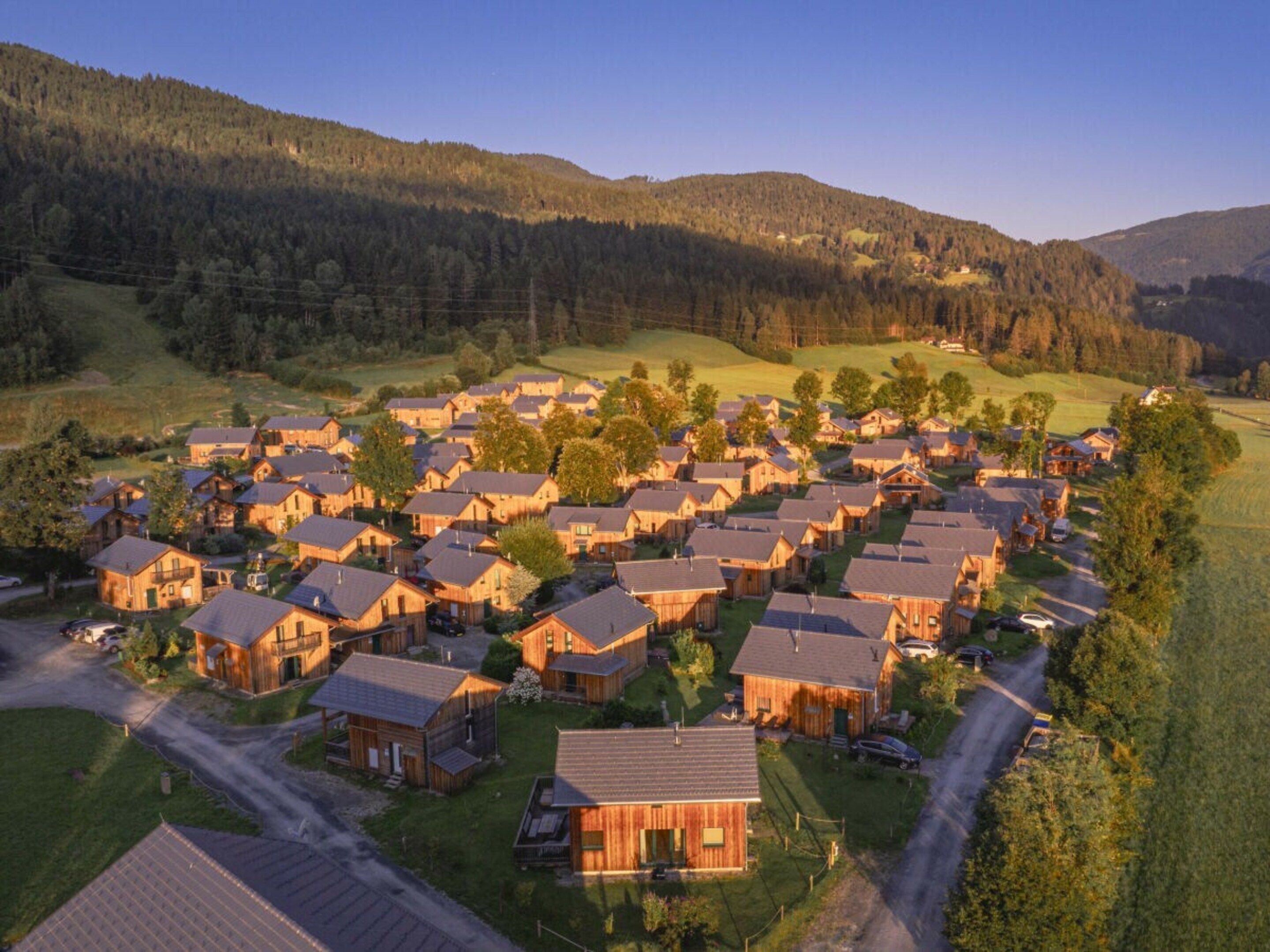 Ein Wohngebiet mit mehreren Holzhäusern, Straßen und einer hügeligen Landschaft im Hintergrund.