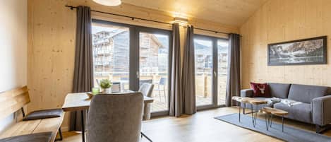 Una habitación amplia con techo de madera, un sofá, una mesa de comedor con sillas y vistas a un paisaje montañoso a través de amplios ventanales.